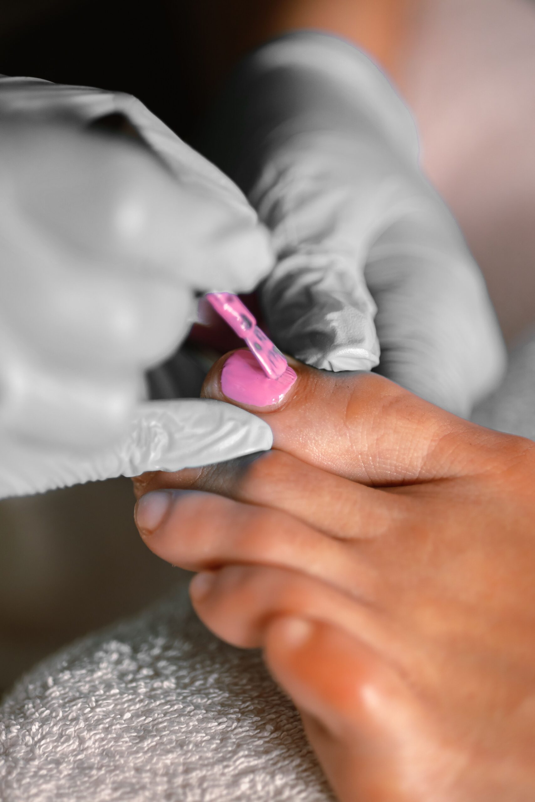 Beautician applying pink nail polish during professional pedicure treatment at spa salon
