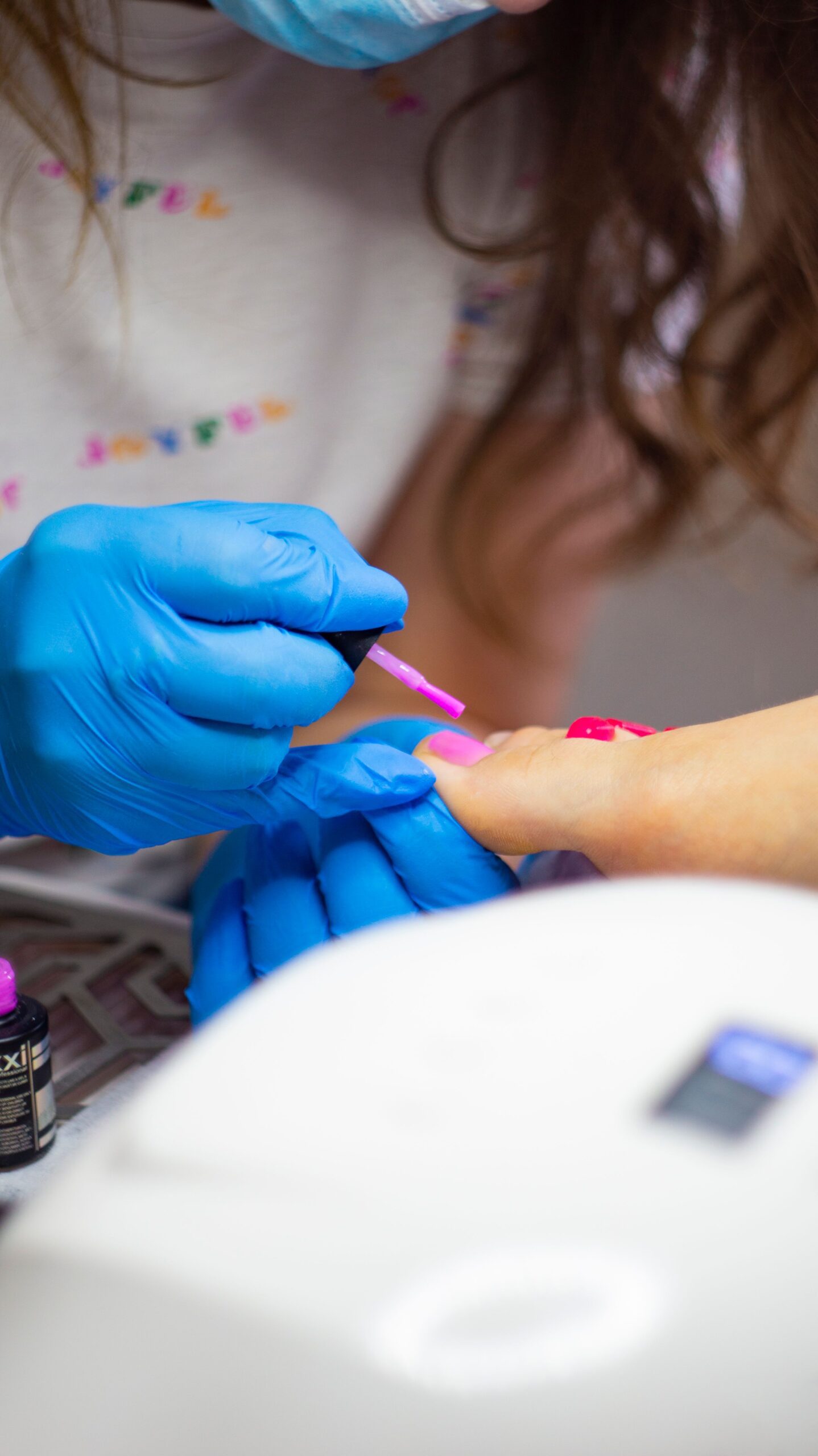 Detailed close-up of professional pedicure session with blue gloves applying pink nail polish precisely