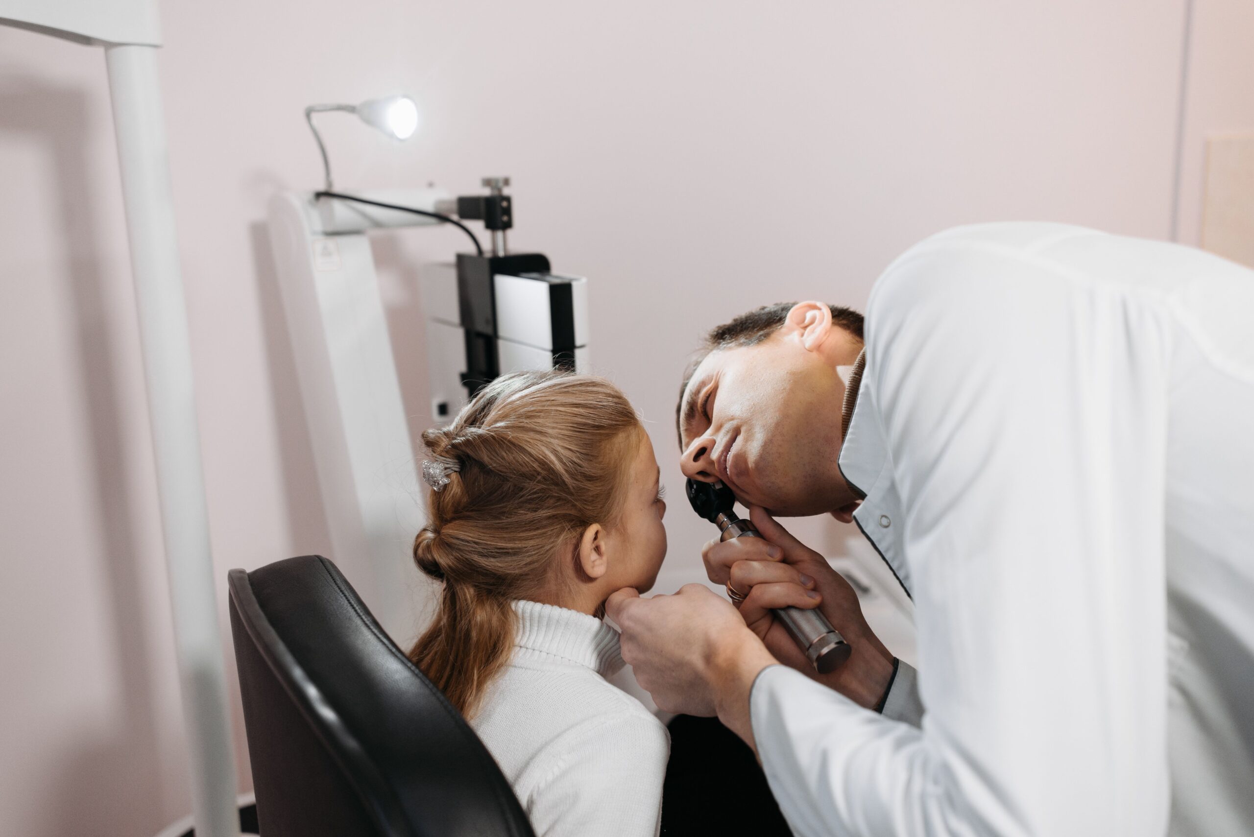 ENT doctor examining young patient ear with otoscope in pediatric medical clinic