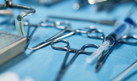 Close-up of hand surgery instruments including scissors, forceps and syringe arranged on blue sterile surgical cloth in operating room