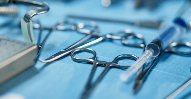 Close-up of hand surgery instruments including scissors, forceps and syringe arranged on blue sterile surgical cloth in operating room