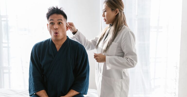 Physician conducting thorough ear examination using otoscope on patient in medical office