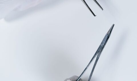 Gloved hand holding surgical forceps close-up on white background