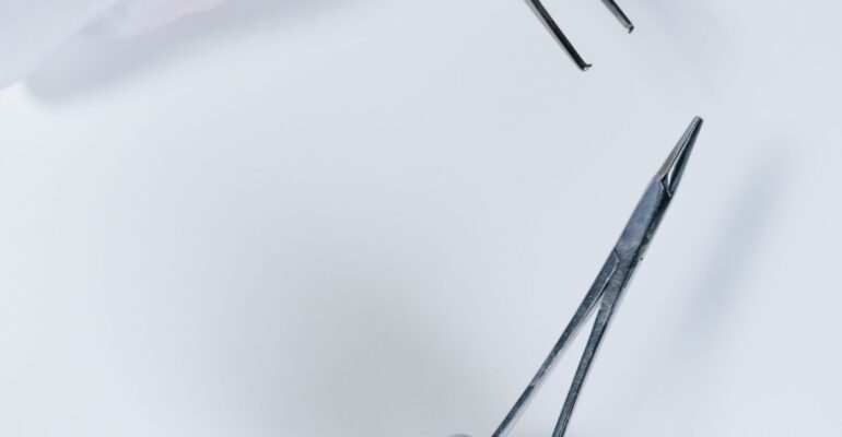 Gloved hand holding surgical forceps close-up on white background